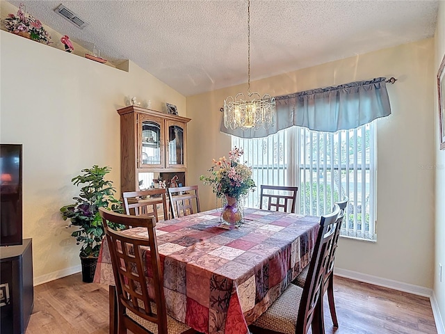 dining space with a textured ceiling, visible vents, an inviting chandelier, and light wood-style floors