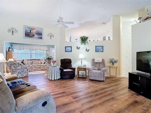 living area featuring a ceiling fan, a high ceiling, wood finished floors, baseboards, and visible vents