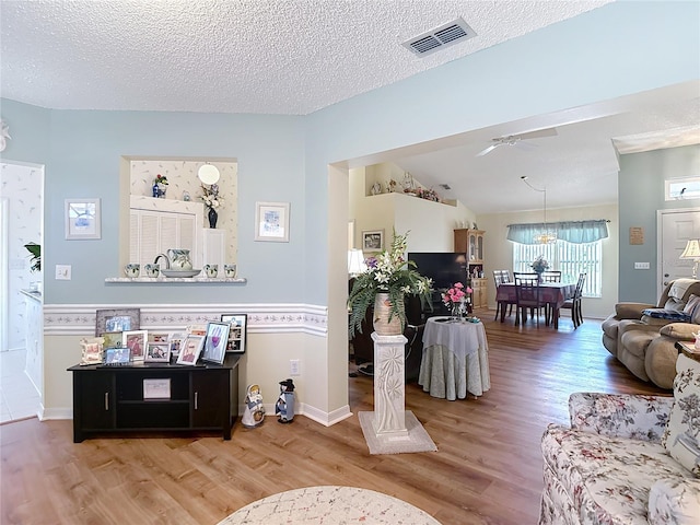 living room with lofted ceiling, ceiling fan with notable chandelier, a textured ceiling, visible vents, and wood finished floors