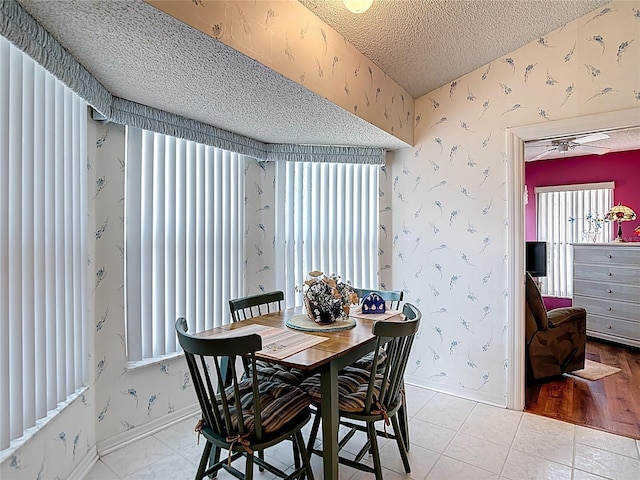 dining space with wallpapered walls, light tile patterned floors, baseboards, and a textured ceiling