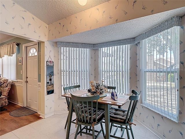 dining space with baseboards, a textured ceiling, wallpapered walls, and light tile patterned floors