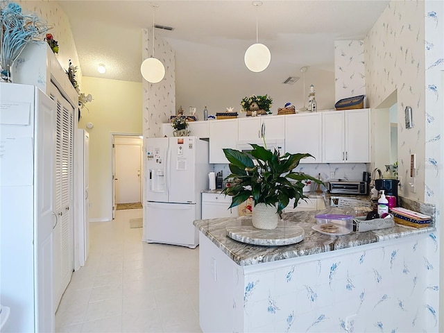 kitchen with a peninsula, white fridge with ice dispenser, white cabinetry, light stone counters, and hanging light fixtures