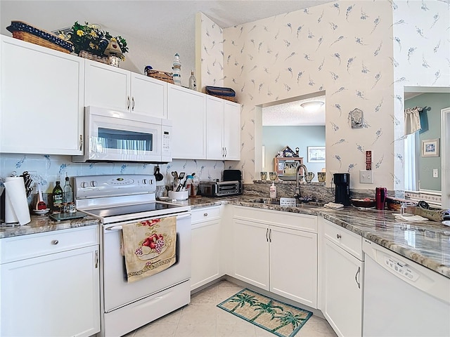 kitchen with white appliances, wallpapered walls, a sink, and light tile patterned floors