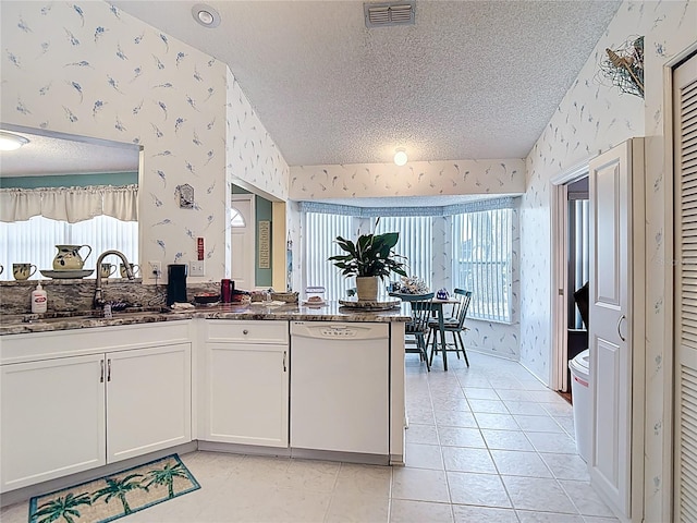 kitchen with a sink, dishwasher, lofted ceiling, visible vents, and wallpapered walls