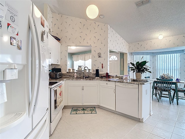 kitchen featuring a textured ceiling, a peninsula, visible vents, white appliances, and wallpapered walls