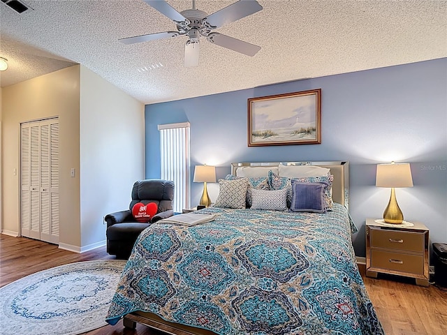 bedroom featuring wood finished floors, a textured ceiling, baseboards, visible vents, and ceiling fan
