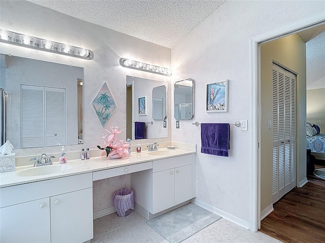 full bathroom with double vanity, a sink, baseboards, and a textured ceiling