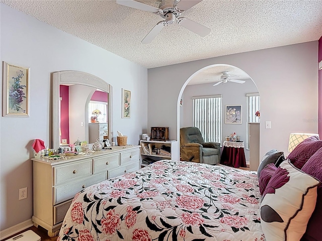 bedroom with arched walkways, baseboards, ceiling fan, and a textured ceiling