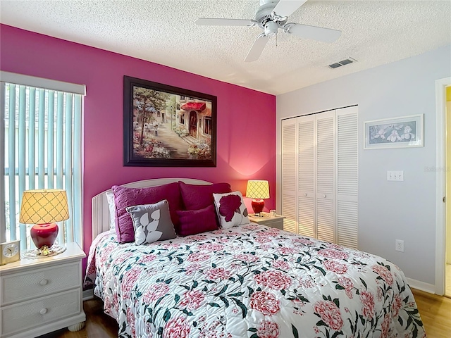 bedroom featuring a closet, a ceiling fan, wood finished floors, a textured ceiling, and visible vents