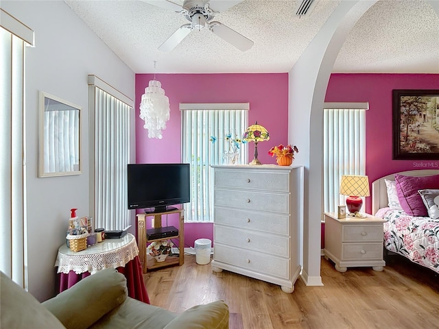 bedroom featuring arched walkways, a textured ceiling, visible vents, and wood finished floors