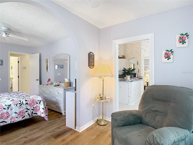 bedroom featuring light wood finished floors, baseboards, arched walkways, and a textured ceiling