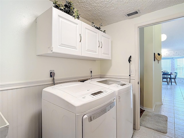 clothes washing area with a textured ceiling, visible vents, cabinet space, washing machine and dryer, and wainscoting
