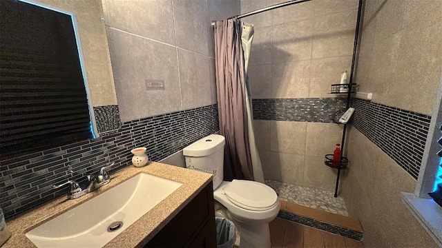 bathroom with tile walls, tiled shower, toilet, vanity, and decorative backsplash