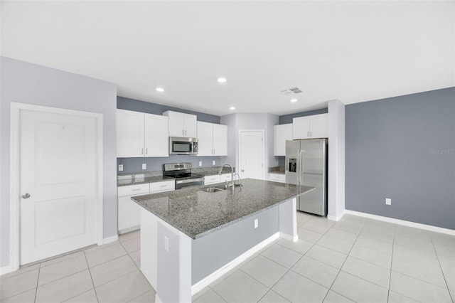 582 Royal Empress Dr, Ruskin, FL 33570 - kitchen featuring appliances with stainless steel finishes, a center island with sink, white cabinetry, dark stone countertops, and light tile patterned floors