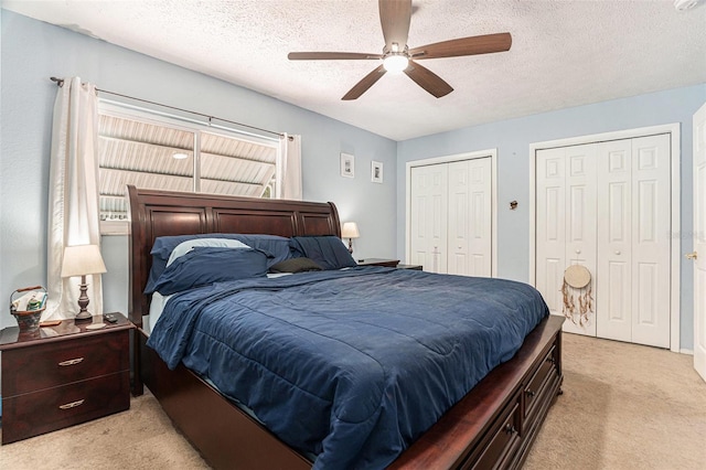bedroom with multiple closets, a ceiling fan, light carpet, and a textured ceiling