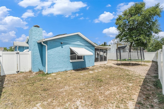 back of house featuring a sunroom, a fenced backyard, a chimney, a gate, and a trampoline