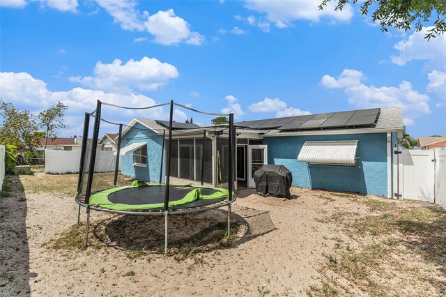 rear view of house featuring a fenced backyard, a trampoline, stucco siding, and roof mounted solar panels
