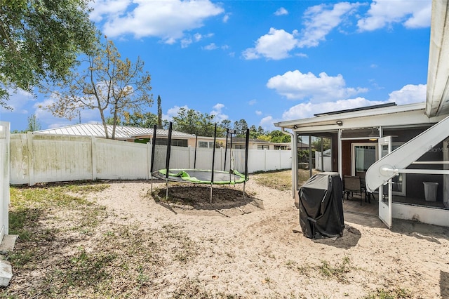 view of yard featuring a fenced backyard, a trampoline, a patio, and a sunroom