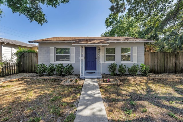 bungalow-style house with roof with shingles, fence, and brick siding