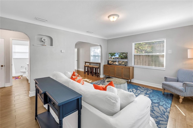 living room featuring visible vents, baseboards, arched walkways, and wood finished floors