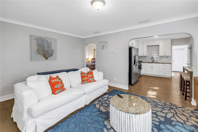 living room featuring arched walkways, baseboards, and wood finished floors