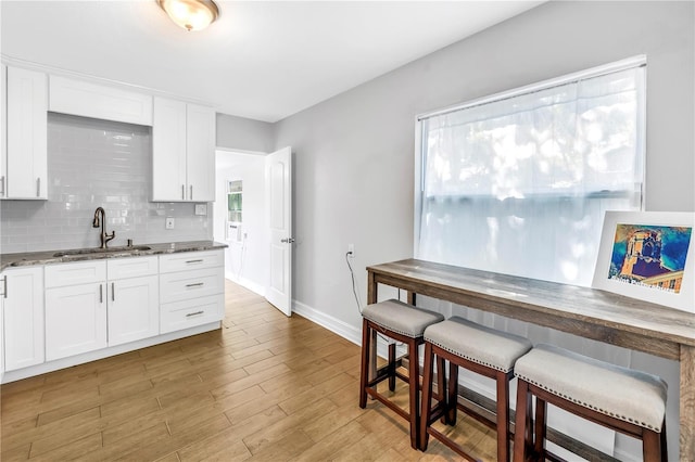 kitchen with dark stone countertops, white cabinets, a sink, light wood finished floors, and backsplash