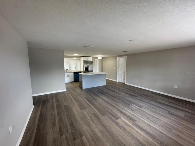 unfurnished living room featuring a sink, a textured ceiling, baseboards, visible vents, and dark wood-style floors