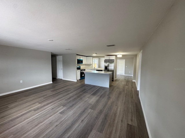 unfurnished living room with baseboards, dark wood-type flooring, a textured ceiling, and visible vents