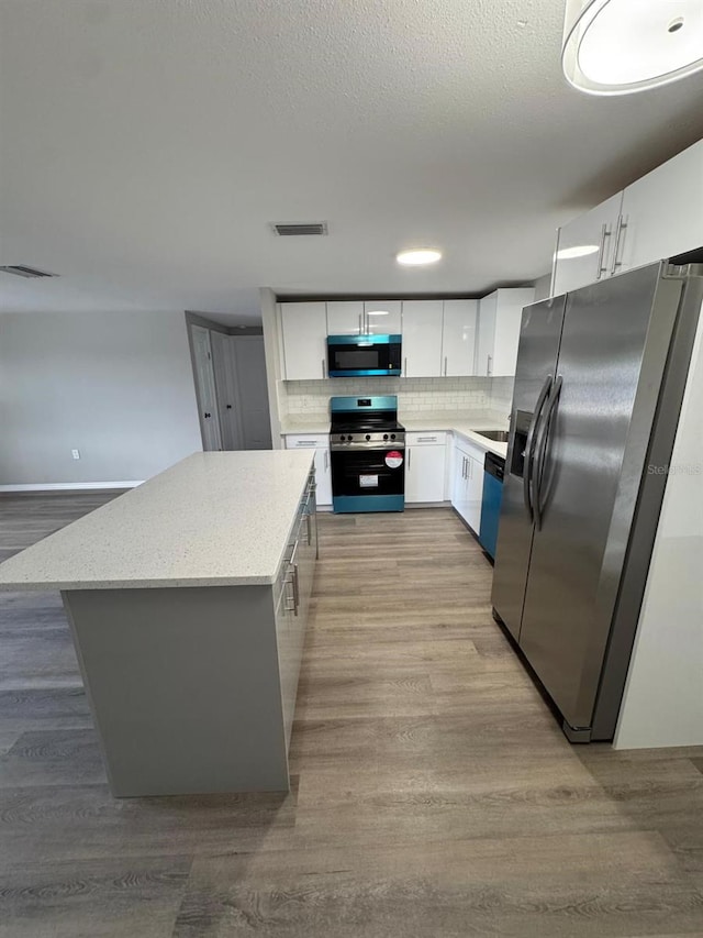 kitchen featuring visible vents, wood finished floors, white cabinetry, tasteful backsplash, and stainless steel appliances