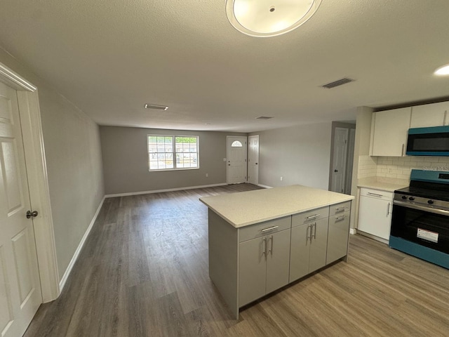 kitchen with stainless steel electric range oven, decorative backsplash, wood finished floors, a kitchen island, and visible vents