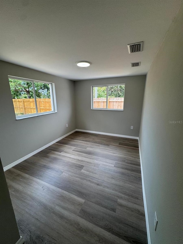 unfurnished room with visible vents, a wealth of natural light, and dark wood-type flooring