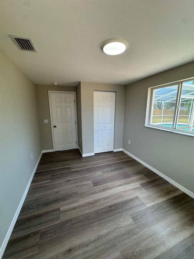 unfurnished bedroom with baseboards, a closet, dark wood-style flooring, and visible vents