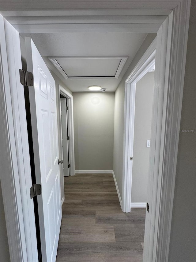 hallway featuring baseboards, wood finished floors, and attic access