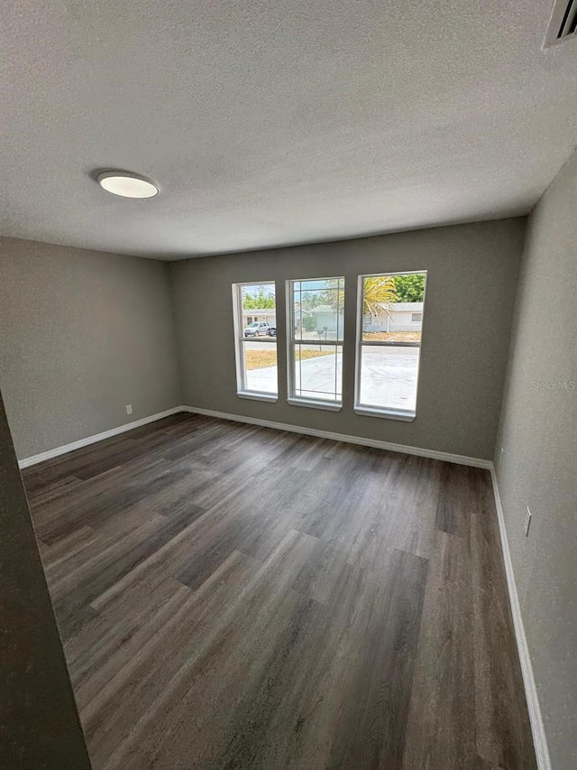 unfurnished room featuring baseboards, dark wood finished floors, a textured ceiling, and visible vents
