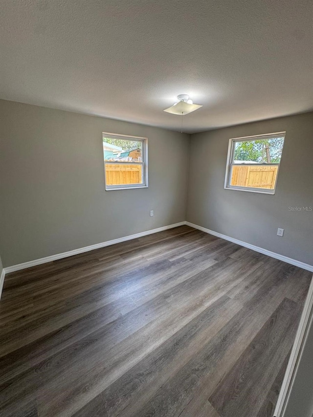 spare room featuring baseboards, dark wood finished floors, and a textured ceiling