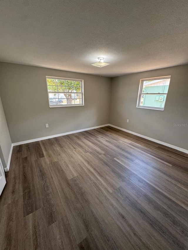empty room with baseboards, dark wood-style flooring, a textured ceiling, and a wealth of natural light