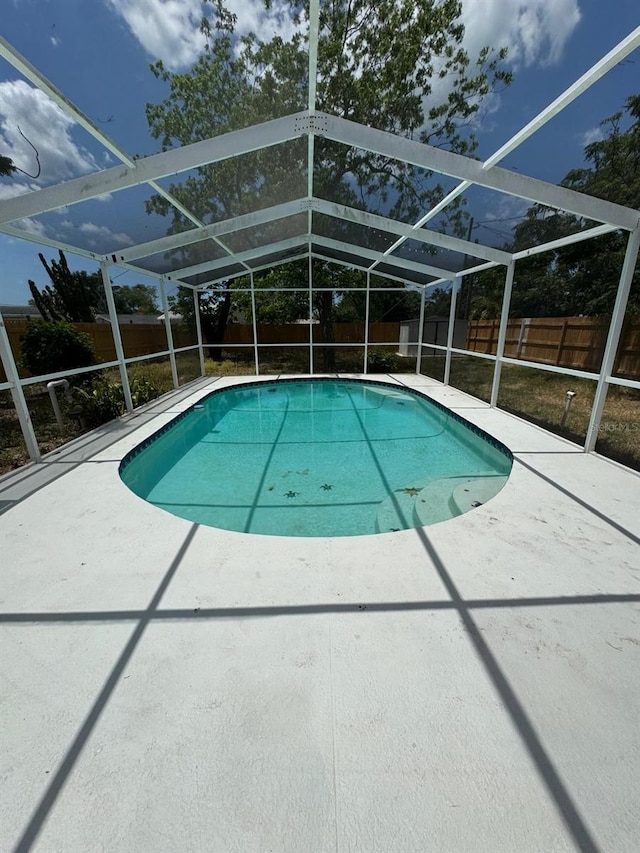view of swimming pool featuring glass enclosure, a fenced in pool, a fenced backyard, and a patio area