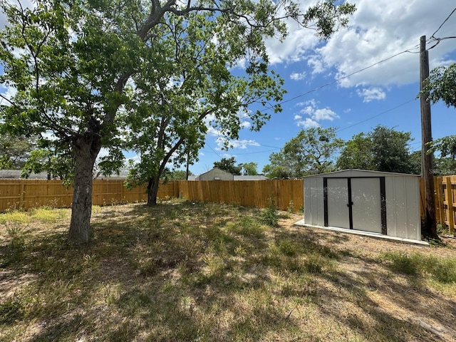 view of yard with a fenced backyard, a storage unit, and an outbuilding