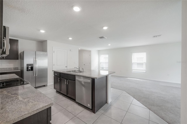 kitchen with visible vents, a sink, appliances with stainless steel finishes, a kitchen island with sink, and light carpet