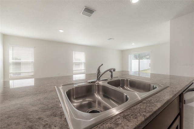 kitchen with light stone countertops, visible vents, a textured ceiling, and a sink