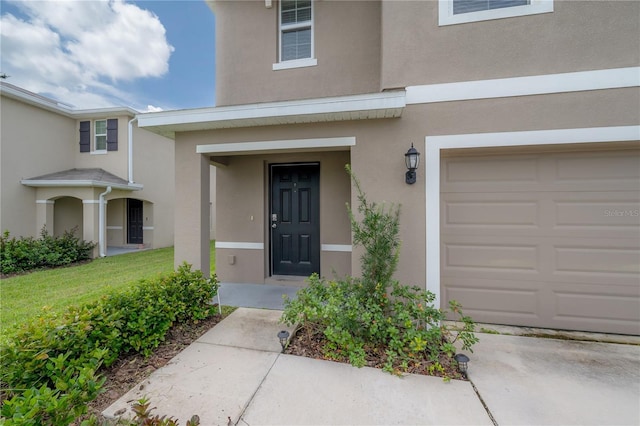 entrance to property featuring an attached garage, a lawn, and stucco siding
