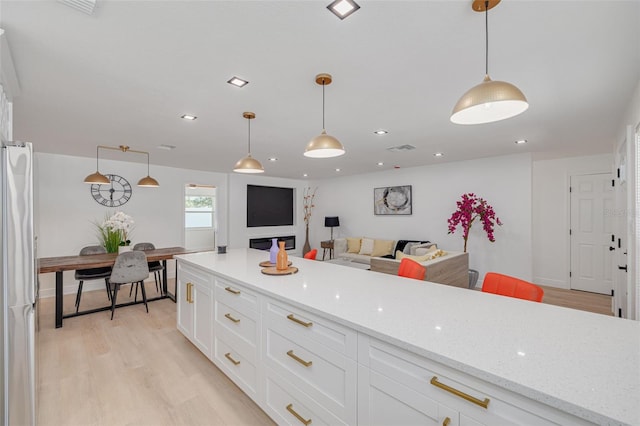 1717 Thames St, Clearwater, FL 33755 - kitchen with freestanding refrigerator, white cabinetry, light wood finished floors, recessed lighting, and light stone countertops