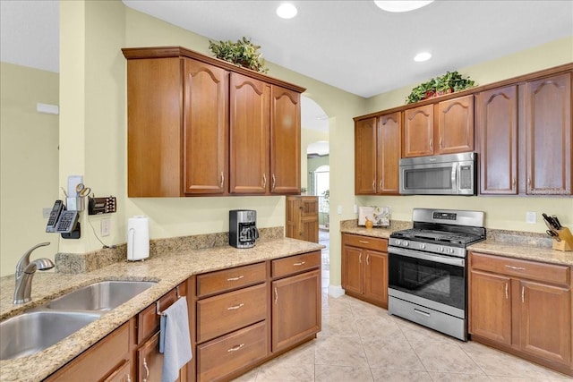 8202 Pinewood Run Ct, Tampa, FL 33647 - kitchen featuring appliances with stainless steel finishes, a sink, arched walkways, light tile patterned floors, and light stone counters