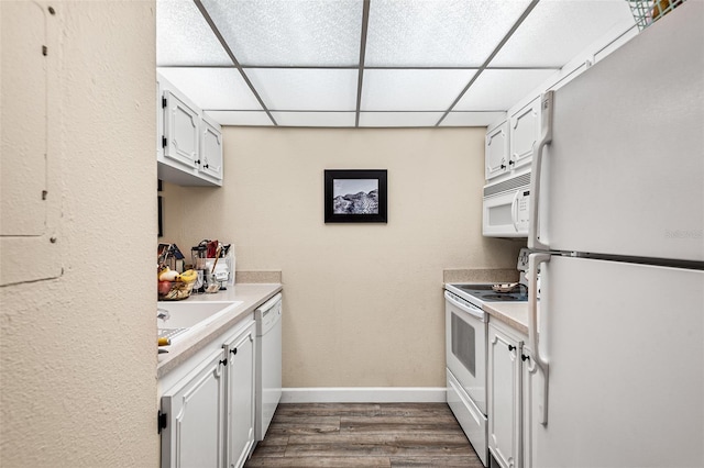 kitchen with light countertops, a sink, dark wood-type flooring, white appliances, and baseboards