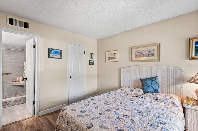 bedroom with wood finished floors, visible vents, baseboards, a textured ceiling, and ensuite bathroom