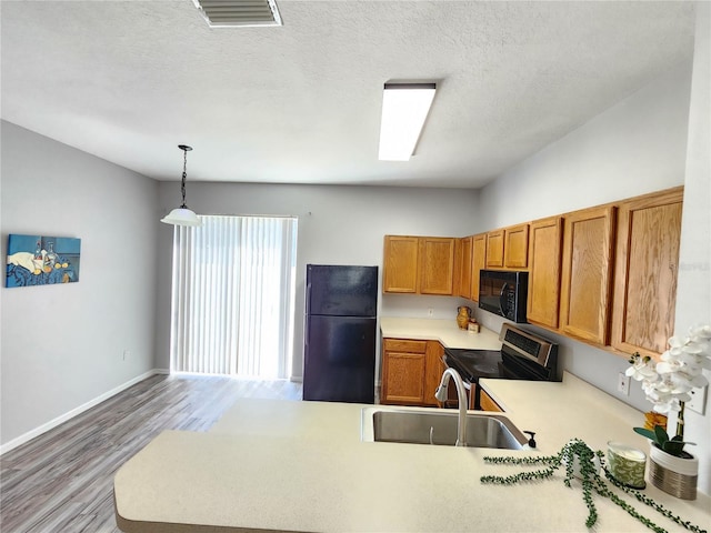 8796 Christie Dr, Largo, FL 33771 - kitchen with black appliances, a sink, light wood-style floors, brown cabinetry, and light countertops