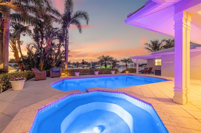 pool at dusk with an outdoor pool, an in ground hot tub, and a patio