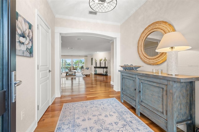 foyer featuring arched walkways, visible vents, crown molding, and wood finished floors