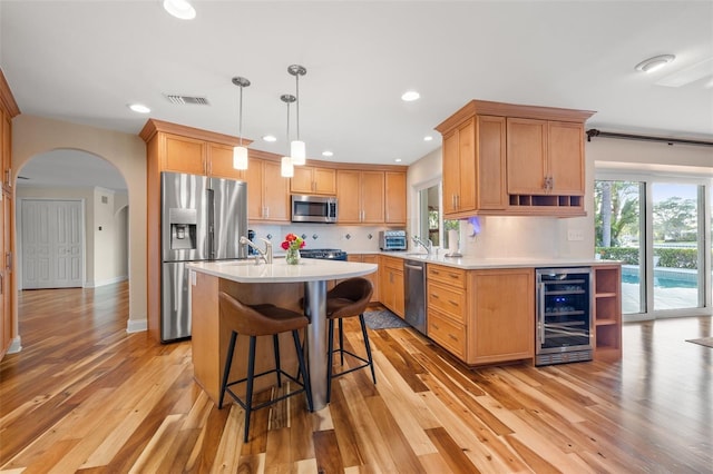 kitchen featuring light countertops, light wood-style floors, stainless steel appliances, arched walkways, and beverage cooler