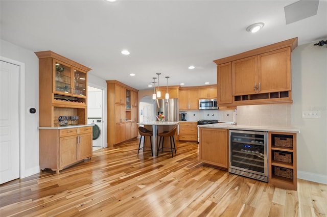 kitchen featuring light wood-style floors, stacked washer and dryer, beverage cooler, stainless steel appliances, and a breakfast bar area